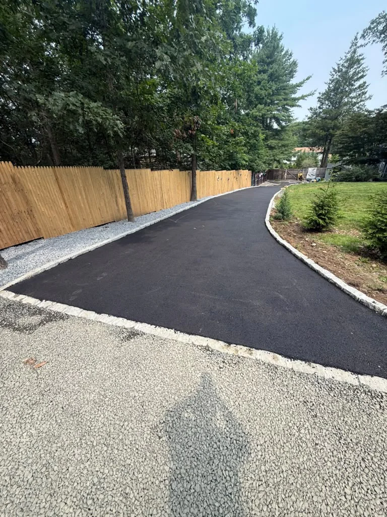 Long curved residential asphalt driveway lined with Belgian block granite curbing along wood fence in Connecticut