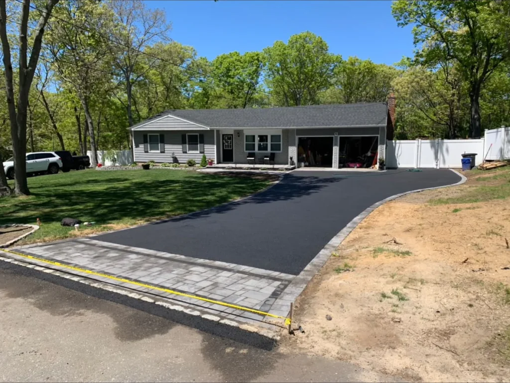 Curved residential asphalt driveway with paver apron and Belgian block cobblestone edging leading to two-car garage