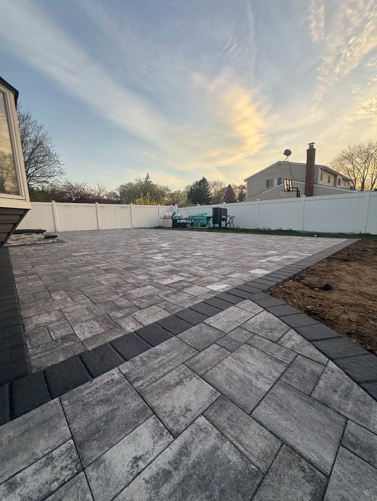 Custom stone paver patio installation with dark soldier course border and patio steps under evening sky