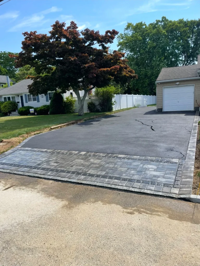 Residential asphalt driveway with custom grey paver apron and border leading to detached garage