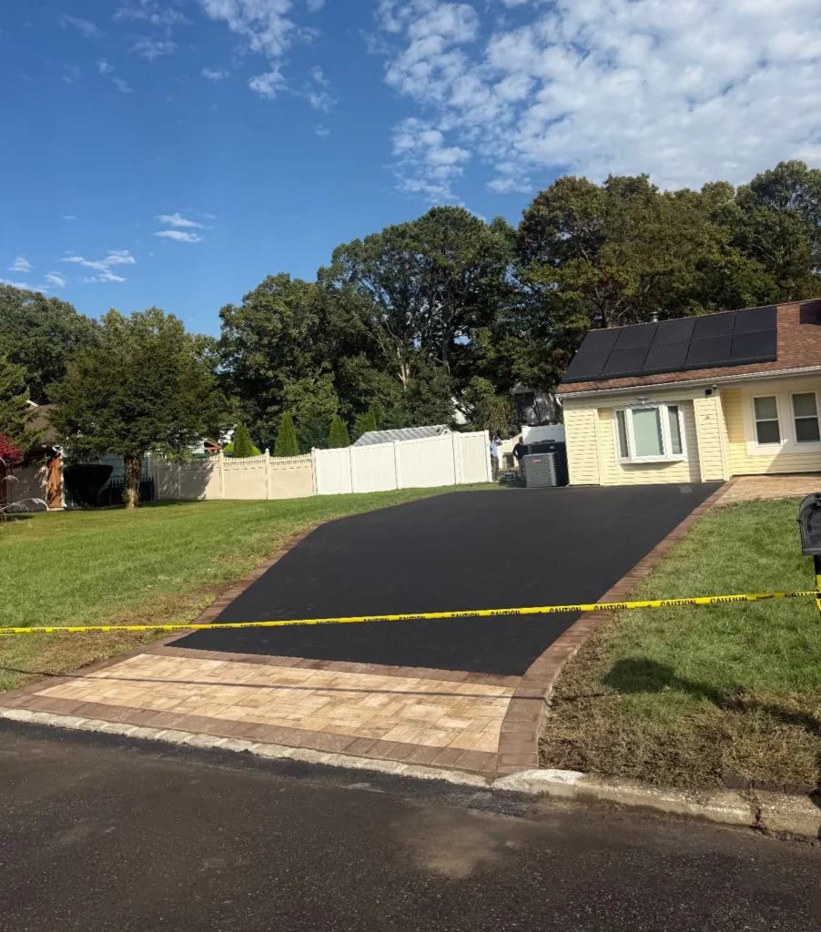 Freshly paved asphalt driveway with tan paver apron and Belgian block borders at yellow suburban home