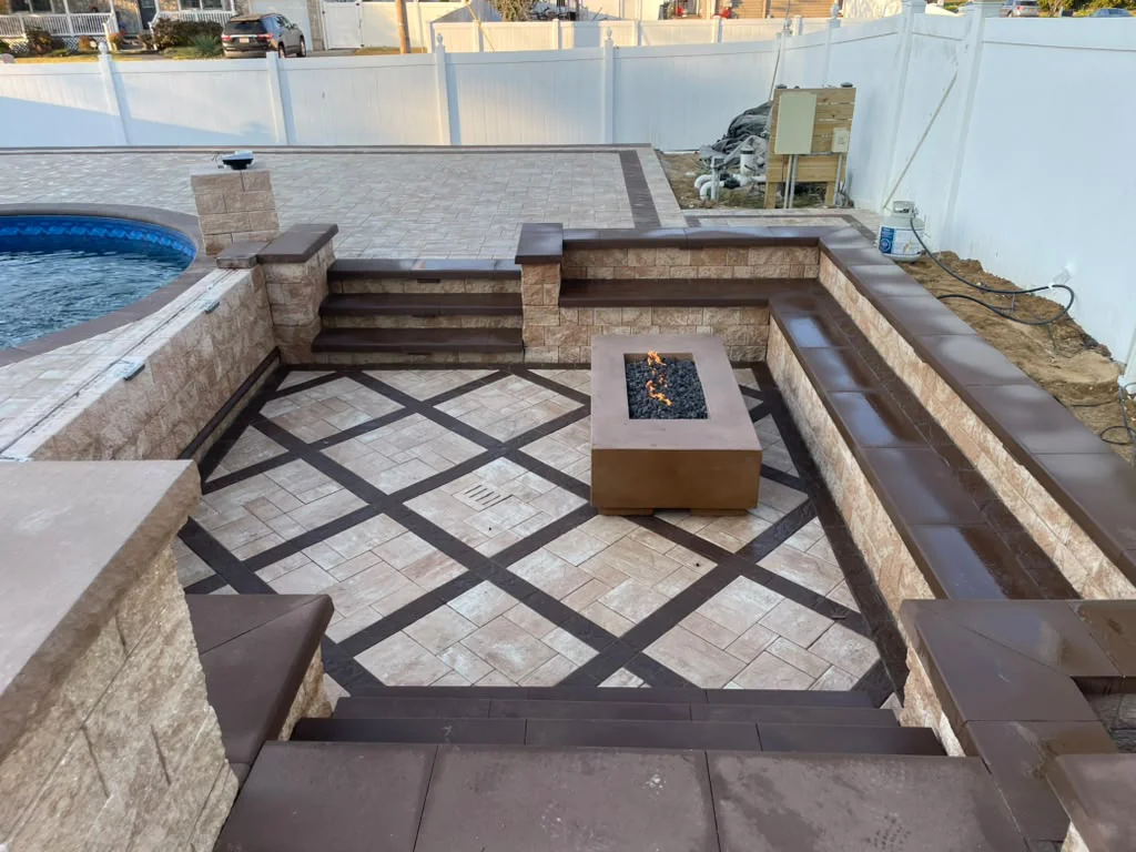 Sunken outdoor patio with custom stone gas fire pit built-in masonry seating walls and diamond pattern pavers next to pool