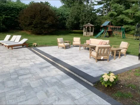 Luxury multi-tiered paver patio with dark step border outdoor lounge furniture and landscaped backyard in Connecticut